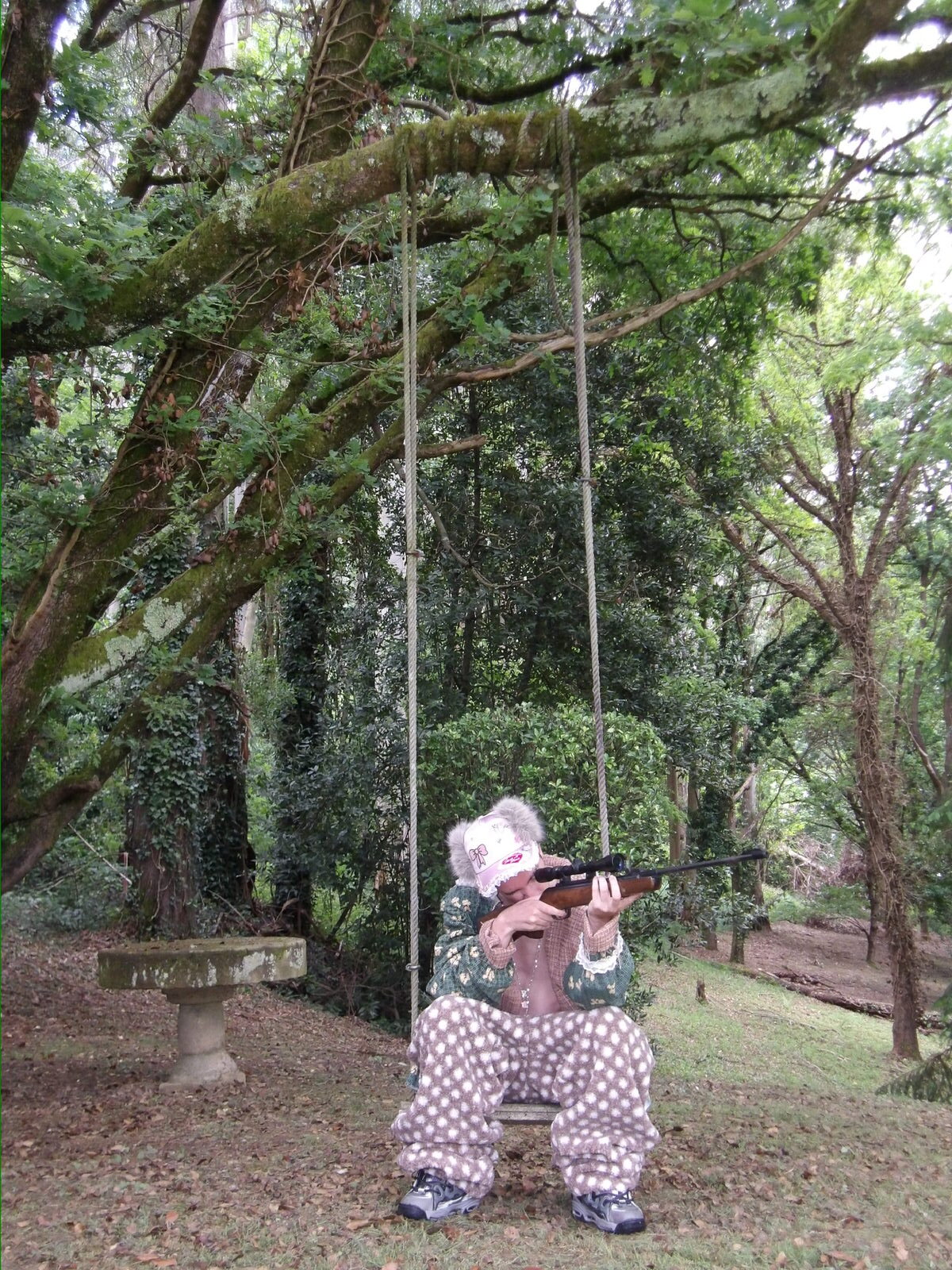 Modelo con pijama de lunares y rifle, sentado en el bosque